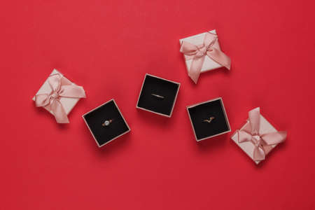 Gold rings in gift boxes on red background. Jewelry shop. Top view