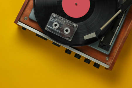 Retro music concept. Vinyl record player with a vinyl record, audio cassette on yellow background....