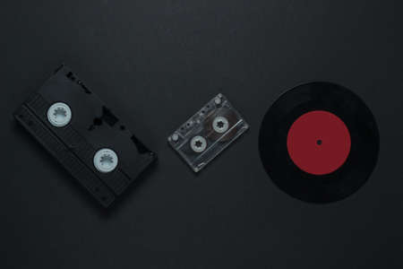 Flat lay retro media and entertainment. Vinyl record, audio cassette, vhs on black background. 80s. Top viewの写真素材