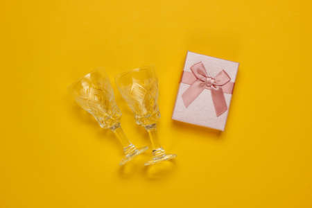 Retro style faceted crystal wine glasses and gift box on yellow background. Christmas concept. Top viewの写真素材