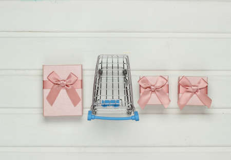 Shopping trolley, gift boxes on white wooden table. Top view