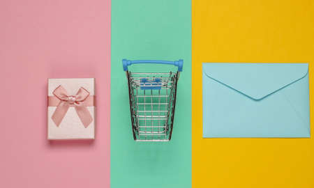 Shopping trolley, gift box, envelope on pastel background. Top view
