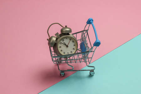Shopping trolley and retro alarm on pink blue pastel background. 11:55 am. New Year.の写真素材