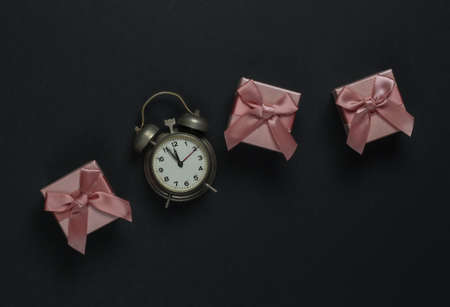 Retro alarm clock and gift boxes with bows on black background. 11:55 am. New Year, Christmas...