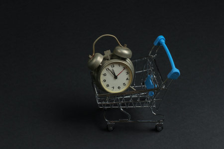 Shopping trolley and retro alarm on black background. 11:55 am. New Year.の写真素材