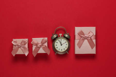 Retro alarm clock and gift boxes with bow on red background. 11:55 am. New Year, Christmas concept....