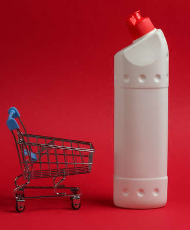 Shopping trolley with white plastic bottle of detergent for the bathroom and toilet on a red background.の写真素材