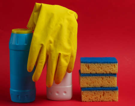 Cleaning concept. Detergent bottles, sponges, gloves on a red background