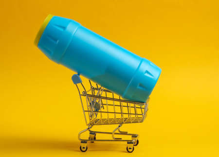 Shopping trolley with white plastic bottle of detergent for the bathroom and toilet on yellow background.の写真素材