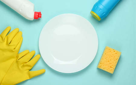 Washing dishes concept. Plate with a sponge and rubber gloves, bottle of detergent on a blue pastel background. Top viewの写真素材