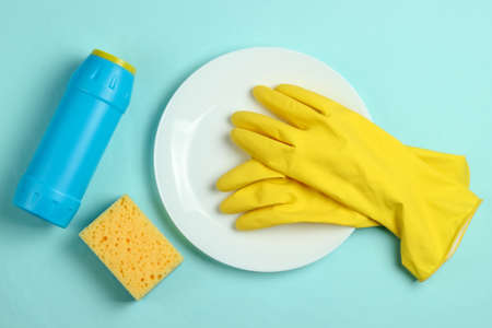 Washing dishes concept. Plate with a sponge and rubber gloves, bottle of detergent on a blue pastel background. Top viewの写真素材