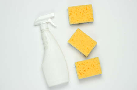 White bottle of spray for cleaning, sponges on white background. Top view. Minimalism