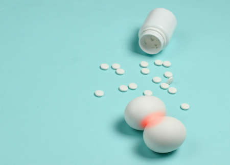 Treatment of prostatitis. Inflammation of the prostate. Allegorical photo of chicken eggs with red inflammation and pills on a blue background.の写真素材