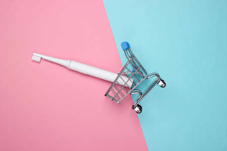 Mini shopping trolley with electric toothbrush on a pink-blue pastel background. Top view.の写真素材