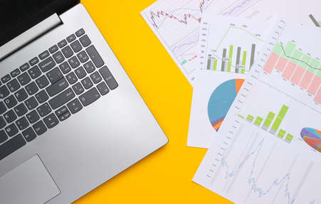 Laptop with graphs and charts on a yellow background. Business plan, financial analytics, statistics. Top viewの写真素材