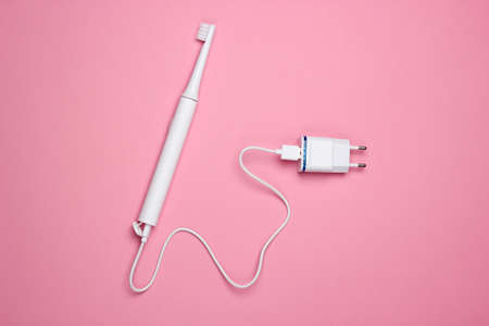 Modern electric toothbrush with a charger on a pink pastel background. Top viewの写真素材