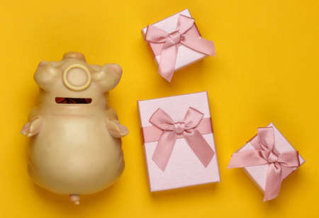 Holiday gifts. Piggy bank with boxes of gifts on a yellow background. Family budget. Top view