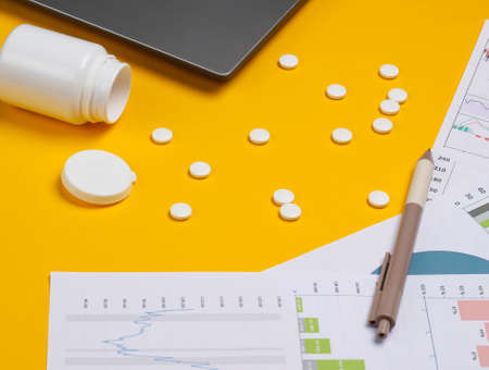 Laptop with pills bottle, graphs and charts on a yellow background. Business plan, financial analytics, medicial statistics.の写真素材
