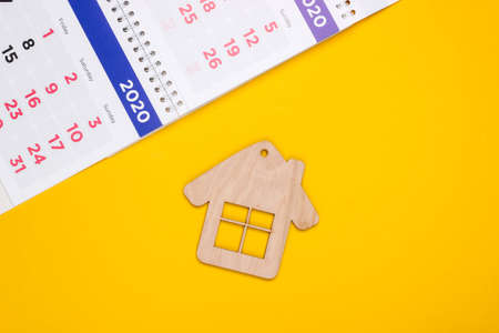 Payment of rent for housing. Mini house figurine with calendar on yellow background. Top view