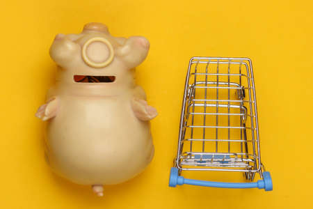 Shopping concept. Piggy bank with shopping trolley on a yellow background. Top viewの写真素材