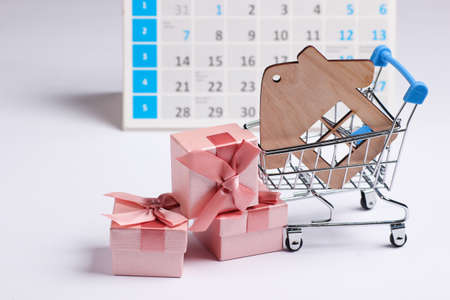 Miniature shopping cart, house figure, gift boxes with desktop calendar on white background. Holiday shopping, black friday, monthly special offer concept. Home purchaseの写真素材