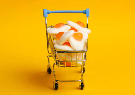 Mini shopping trolley with marmalade fried eggs on a yellow background. Sweets Shopping, Pastel Color Trend, Food Conceptの写真素材