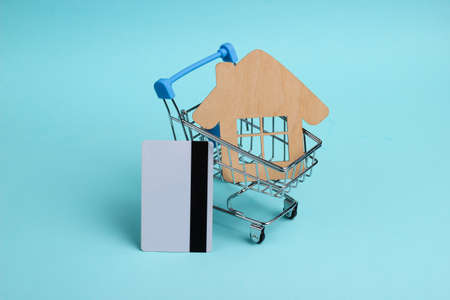 Home purchase concept. Mini shopping trolley, house, credit card on blue pastel background
