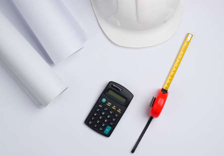 Engineer workspace. Construction helmet, rolls of drawings, calculator and ruler on white...