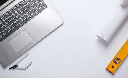 Engineer workspace. Laptop, rolls of drawings, toolson white background. Top view. Copy space