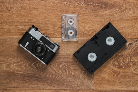 Video cassettes, audio cassette, old-fashioned film camera on the floor. Retro media 80s. Top view