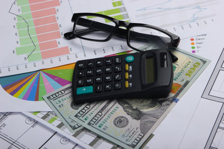 Classic eyeglasses, dollar bills, calculator with graphs and charts. Economic calculation, analytics, business concept.の写真素材
