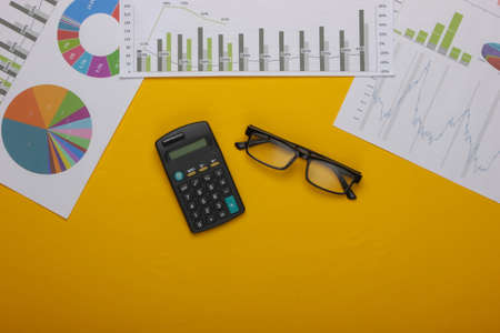 Classic eyeglasses, calculator with graphs and charts on yellow background. Economic calculation, analytics, business concept. Top view. Top viewの写真素材