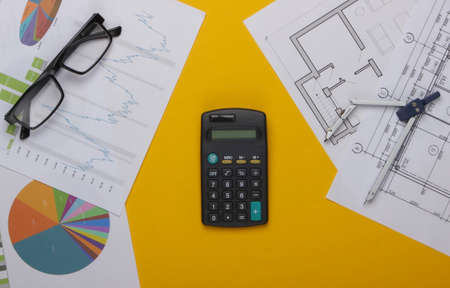 Business analysis in engineering. Graphs and charts, construction plans, calculator, glasses, pair of compasses on a yellow background. Top viewの写真素材