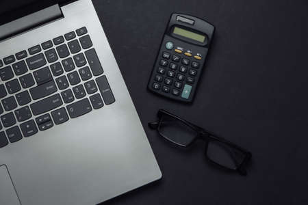 Laptop, glasses, calculator on a black background. Top view.の写真素材