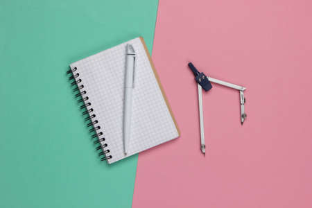 Drawing compass and notebook on pink-blue background. Top view. Stationery. Engineering