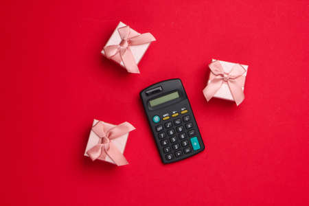 Calculating the value of the gift. Gift boxes and calculator on a red background. Top viewの写真素材