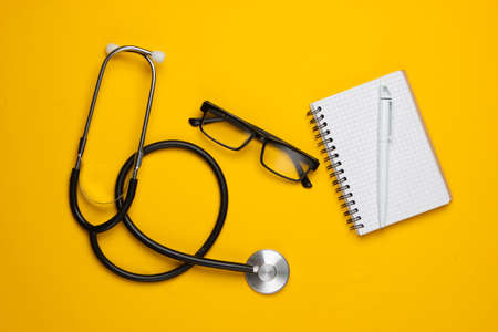 Medical still life on a yellow background. Stethoscope, glasses, notepad. Top viewの写真素材