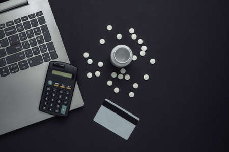 Online purchase of medicines. Bottle of pills, laptop, calculator, bank card on a black background. Top viewの写真素材