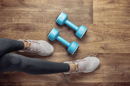 Fitness concept. Female legs in leggings and sports shoes sits on the floor with dumbbells. Top viewの写真素材