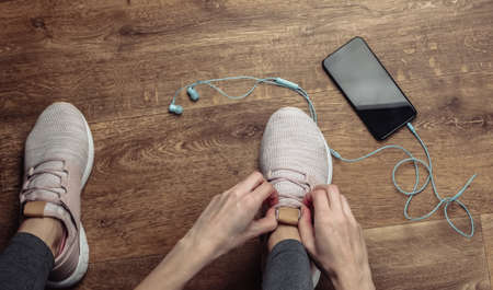Fitness, sport concept. Woman tying shoelaces of sports shoes for running while sitting on the floor...