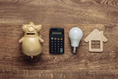Calculator, light bulb, house figure, piggy bank on a wooden floor. Economy, eco concept. Payment for electricity. Save your money. Top viewの写真素材