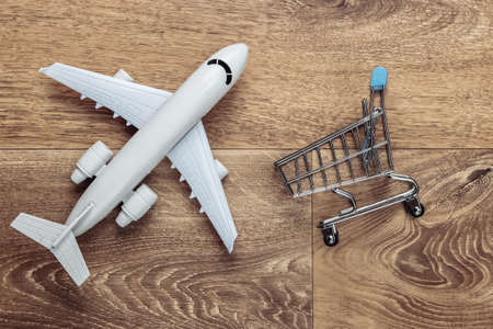 Flat lay composition. Air delivery, shopping, logistics. Figurine of shopping trolley, airplane on wooden floor. Top viewの写真素材