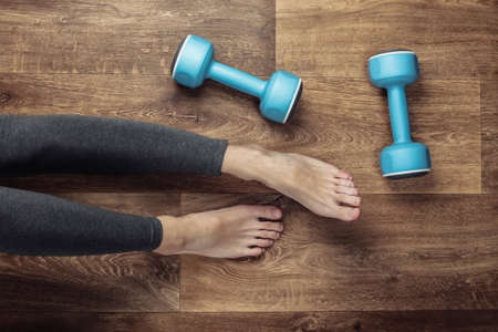 Fitness concept. Female legs in leggings and bare feet sits on the floor with dumbbells. Top viewの写真素材