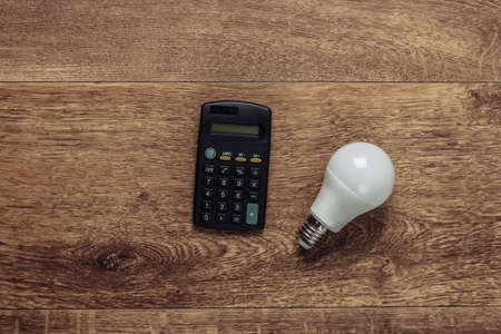 Calculator and light bulb on a wooden floor. Economy, eco concept. Save your money. Top viewの写真素材