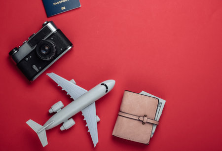 Flat lay travel composition on red background. Plane figurine, passport, wallet with dollars, camera. Recreation, vacation and tourism, minimalism concept. Top viewの写真素材