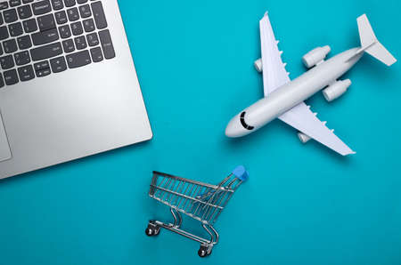 Flat lay composition. Air delivery. Online shopping. Laptop, figurine of shopping trolley, airplane on a blue background. Top viewの写真素材