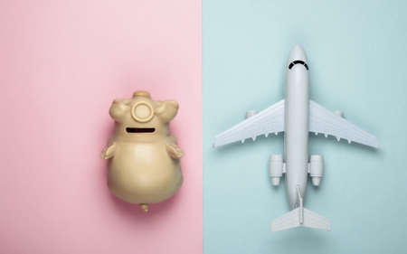 Flat lay travel composition. Plane figurine, piggy bank on pink-blue pastel background. Top viewの写真素材