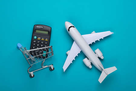 Flat lay composition. Cost calculation of Air delivery, shopping, logistics. Figurine of shopping trolley, airplane, calculator on blue background. Top viewの写真素材