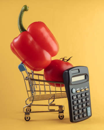 Mini Shopping basket with bell pepper, tomato and calculator on yellow background. Calculation of the cost of purchases in supermarket, economy.の写真素材