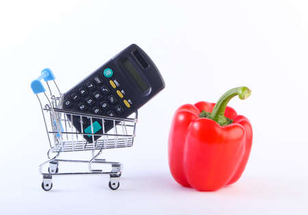 Mini Shopping trolley with bell pepper and calculator on white background. Calculation of the cost of purchases in supermarket, economy.の写真素材
